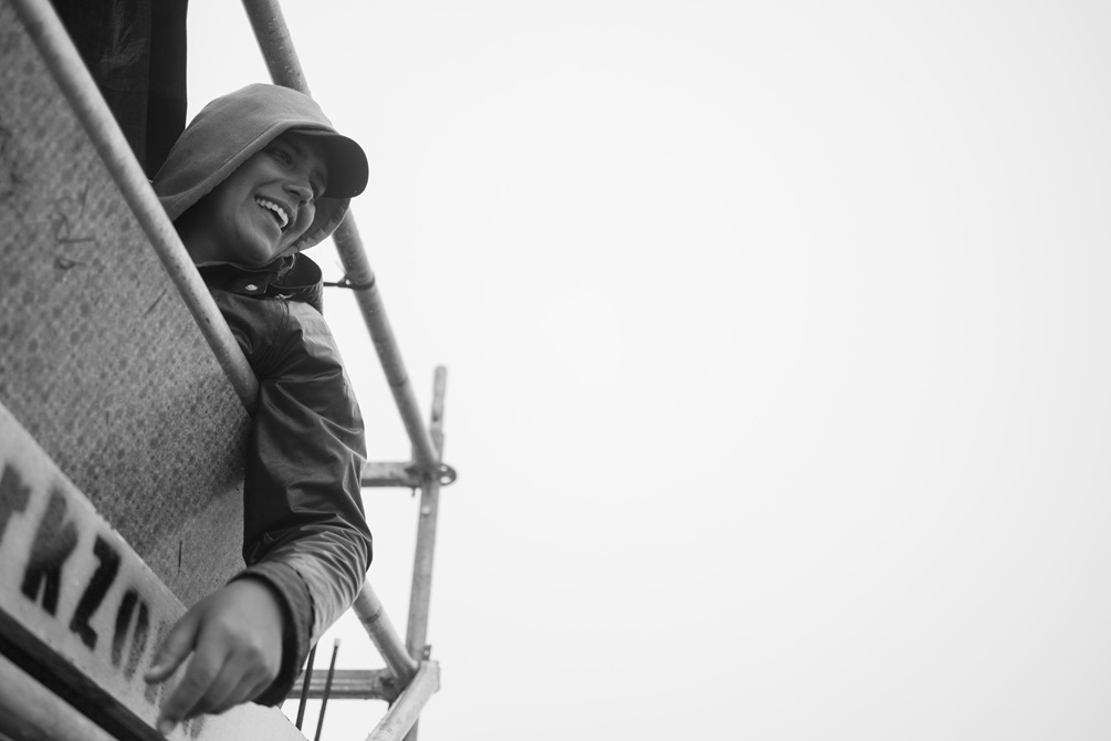Person sitting with an arm hanging out the side of a waka with their hood up.