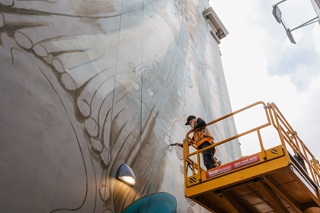 Worker on a lift painting a mural.
