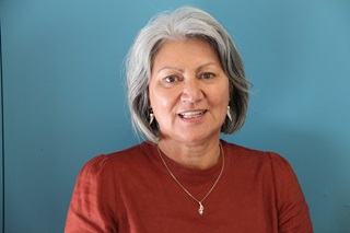 Portrait of Wellington City Council mana whenua representative for Ngāti Toa Rangatira. She is dressed in dark red and wearing a necklace, smiling with a blue wall behind her.