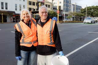 Two workers standing on the street in orange high vis jackets.