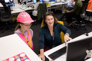 A woman showing a little girl something on a computer screen in the middle of an office.