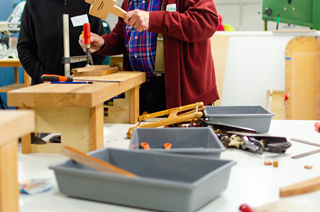 Two people doing woodworks at a table.