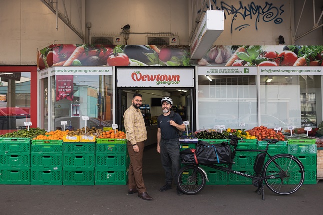 Two people standing outside of a Greengrocer in Newtown with an ebike and veges out front.