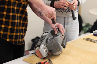 A pair of hands fixing a tool on a bench.