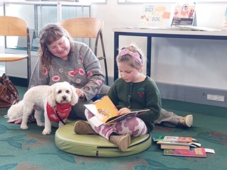 Read to Kurī programme at the library . A young girl reading next to a dog. 