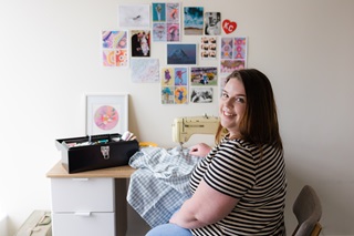 Woman wearing a striped tshirt sitting infront of a sewing machine.