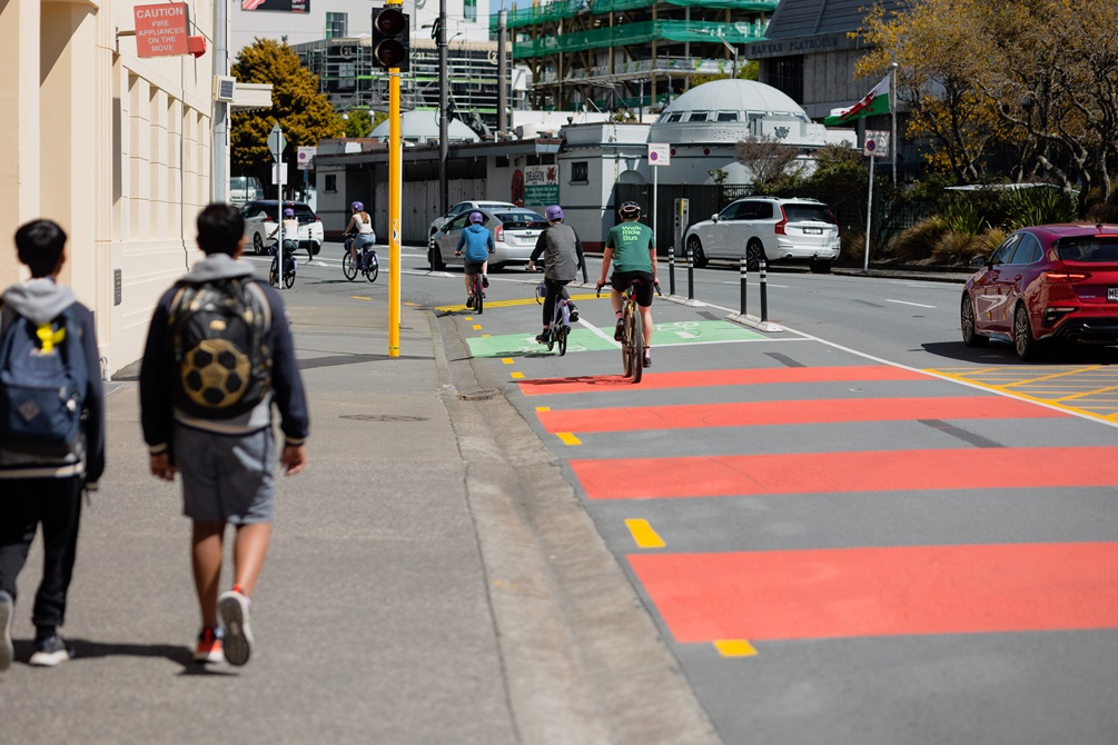 Students walking on the side of the road with people cycling in the lane next to them.