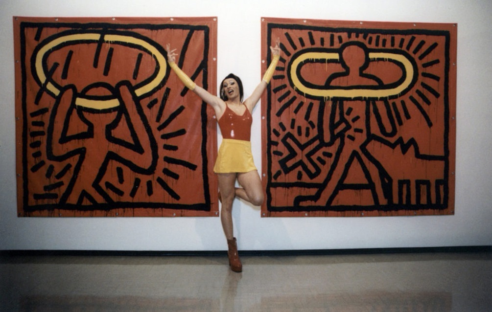 A drag queen posing in front of two large red and black Keith Haring paintings at the opening of his exhibition at City Gallery Wellington.