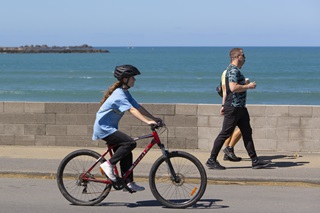 Person cycling down the street alongside the ocean.