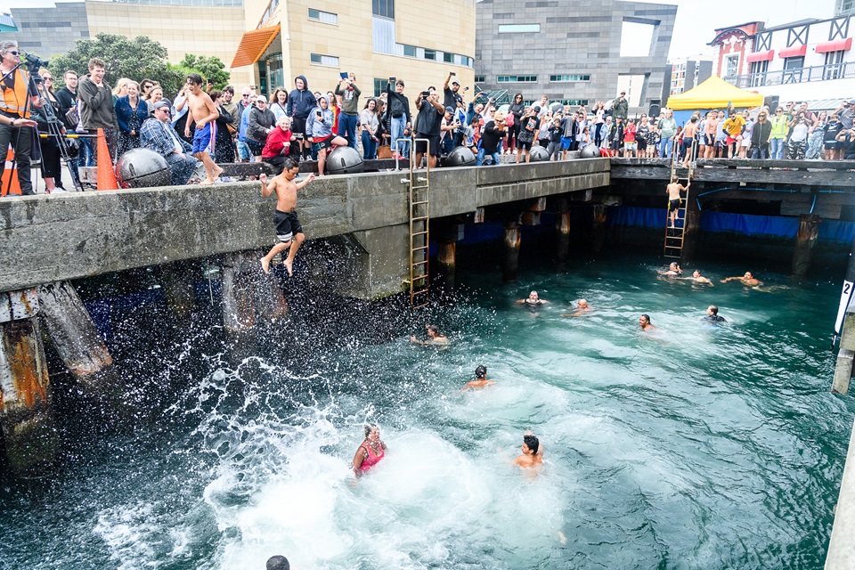 Group of young people jumping into the diving platform water area along Taranaki Wharf