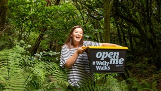 Woman in a stripy top holding a black and yellow box in native bush.