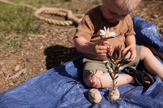 A young boy playing with a flower while sitting on a blue tarpaulin.