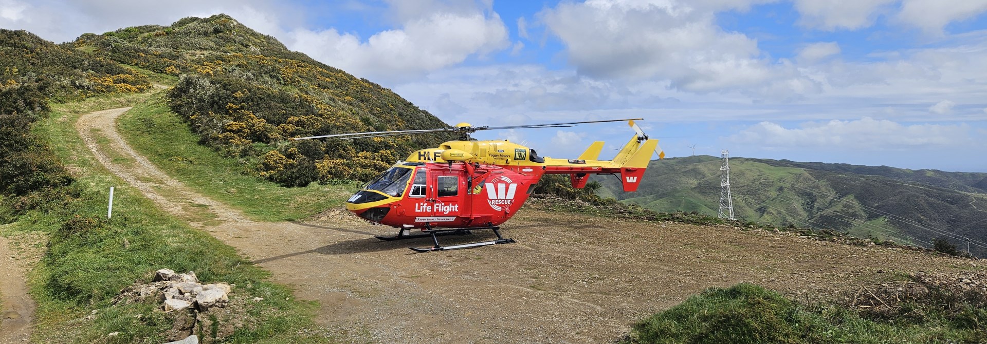 Red and yellow helicopter at the top of a hill with a path leading up to the landing area.