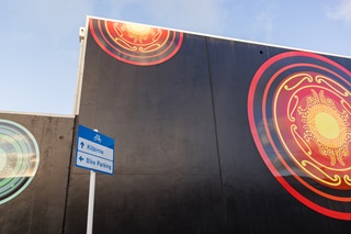 Giant gold, blue and green auripo on a black wall with a bike lane sign infront.
