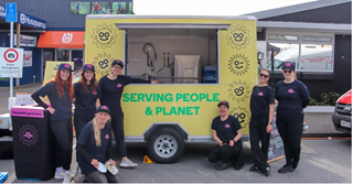 A group of people standing infront of a yellow food truck, all wearing black uniforms.