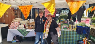 Two people standing infront of market stall with bright yellow bunting strung behind them.