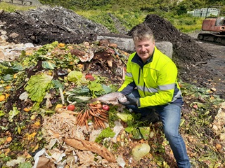 Man in high vis crouching over a pile of compost.