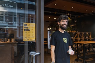 Person standing holding a coffee cup infront of a coffee shop.