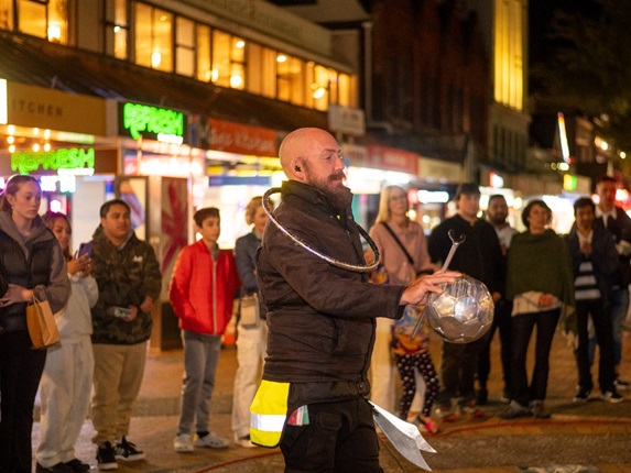 Busker performing on the street with a crowd behind him.