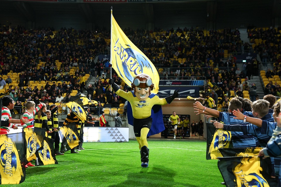 Hurricanes mascot runs on to field and greets fans with players in background.