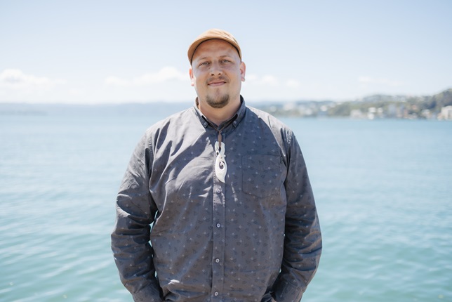 A man in a blue shirt with a cap standing infront of the harbour.