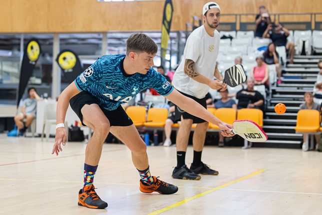 image of Will-Dewhirst-Playing-pickleball. Will is reached out to hit an orange ball with a paddle.