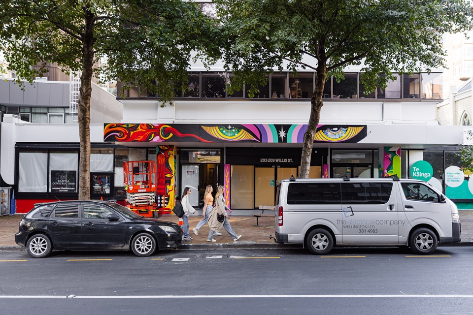 Youth hub entrance from across the road with cars in foreground and mural in progress.