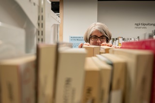 The top of a woman's face peeking out from behind a bookshelf in a library.z