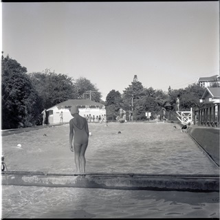 Black and white archive photo of a person climbing into an outdoor pool.
