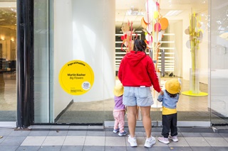 A person with two kids standing infront of a shop window looking at the artwork inside.