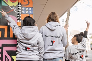 Three people in grey jerseys posing with Te Tai Ohinga branding on their tops.