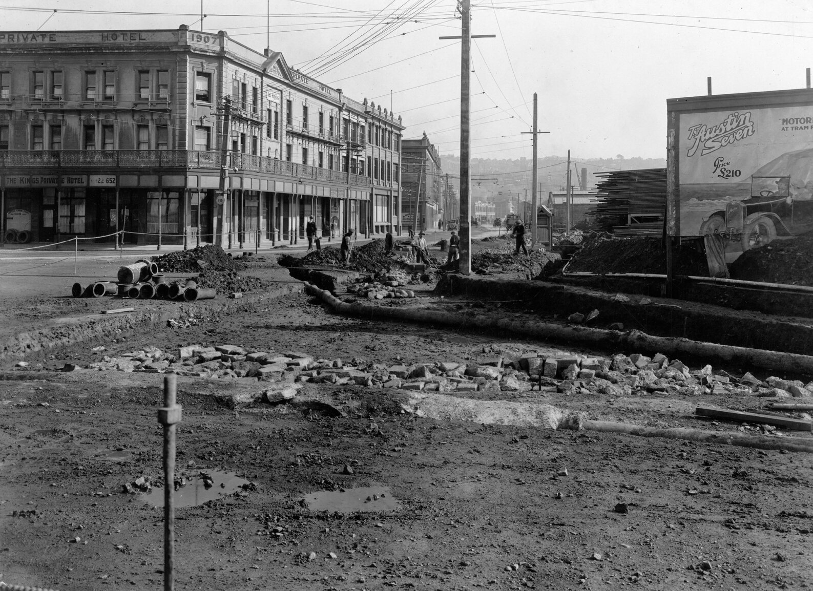 Road works in progress, a billboard advertises 'The Austin Seven, price 210 pound' and the Kings Private Hotel is in the background.
