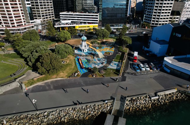 Birds eye view of penguin an area on the waterfront that is being used to create new penguin habitats, with a walkway, playground and buildings in the background.