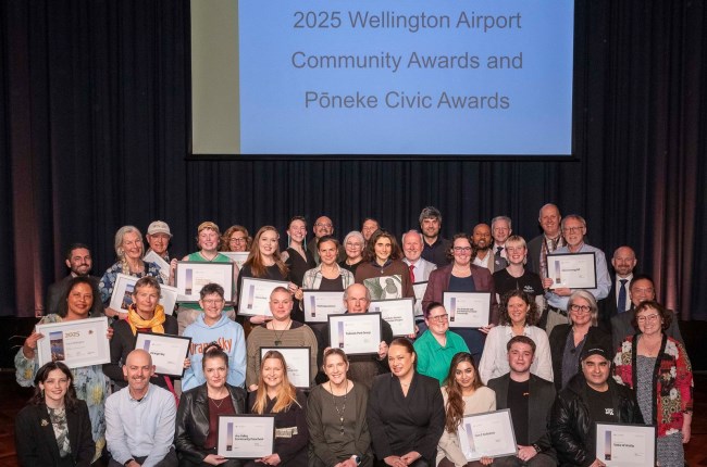 Group photo of winners and nominees with certificates on stage under projection screen display.