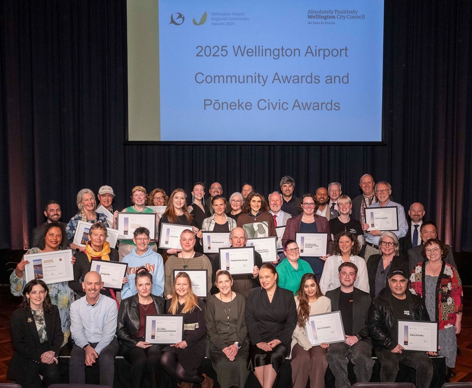 Group photo of winners and nominees with certificates on stage under projection screen display.