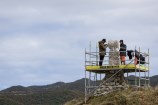 Photo of Ariki and Matahi working on the pou while standing on scaffolding in the wind