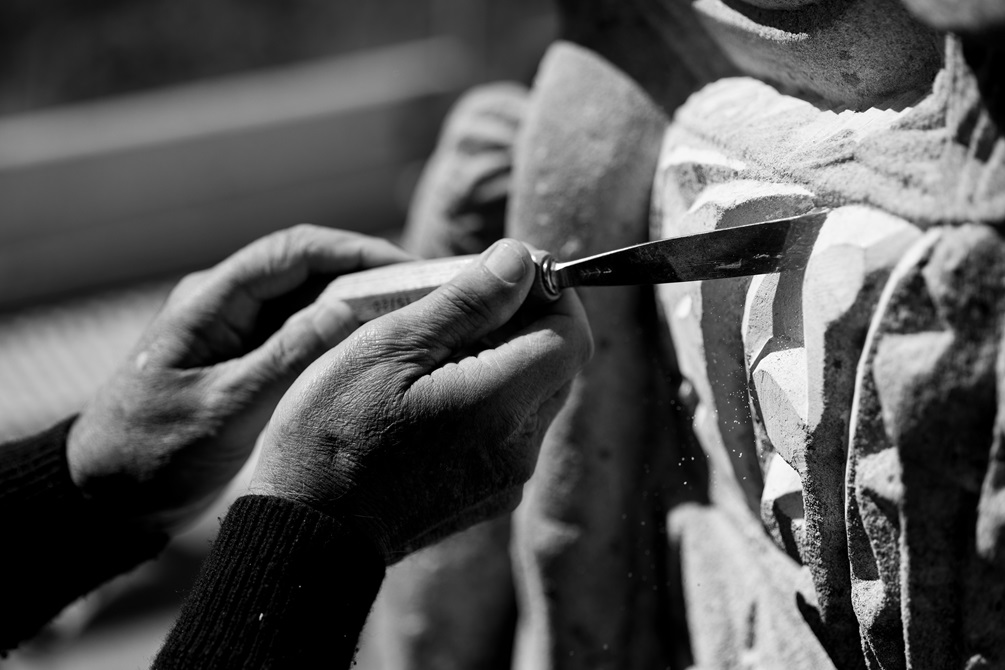 A close-up of a carvers hand while carving into the pouwhenua 