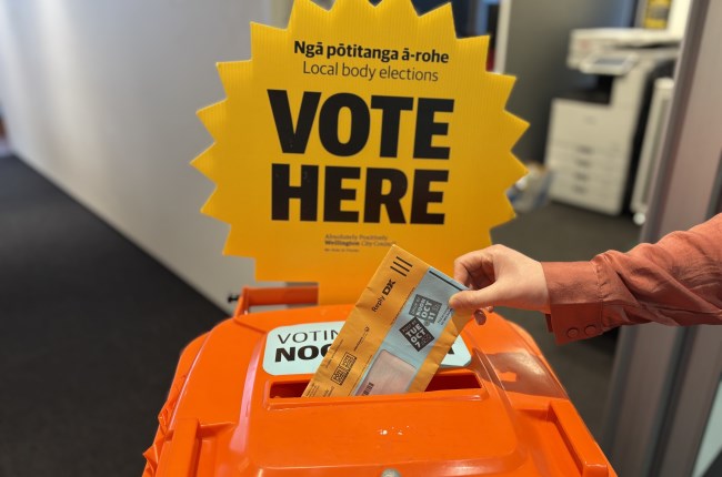 Voting papers being dropped into orange voting bin.