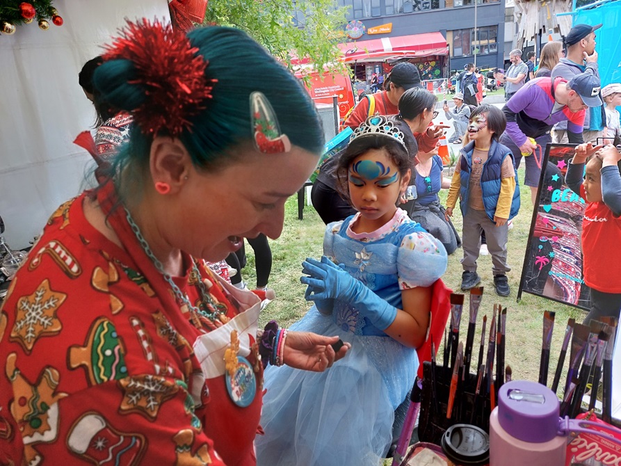 A child getting their face painted at a Christmas event.