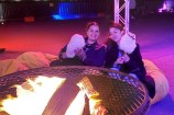 Two young women sit on bean bags in front a roaring brazier. They are both holding large cotton candy sticks.