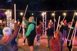 A mix of people holding large sticks and learning to play a traditional Māori game.