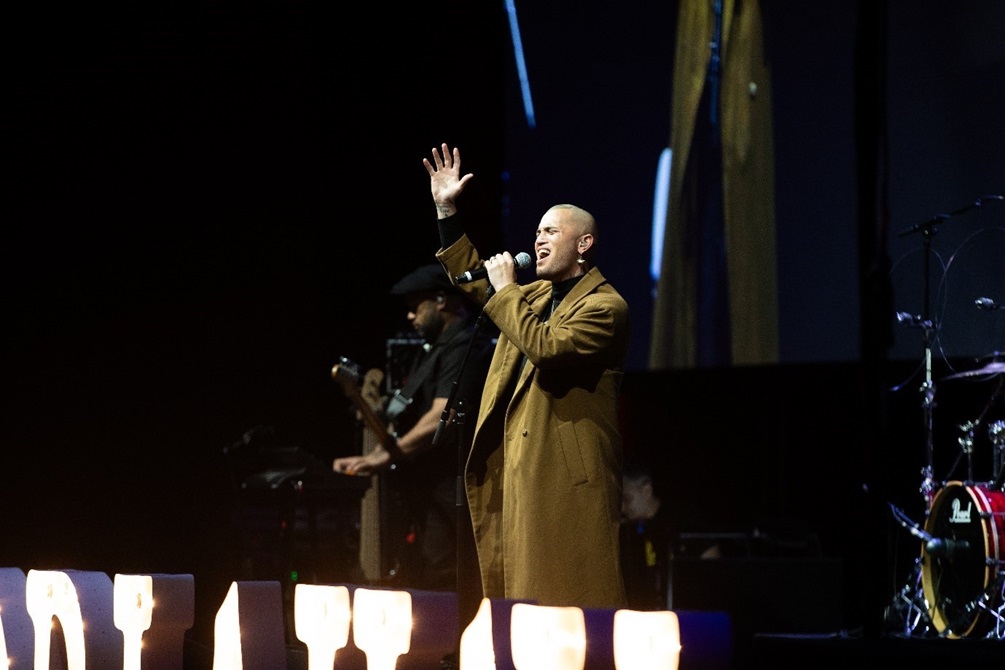 Stan Walker singing on stage and waving to the crowd.