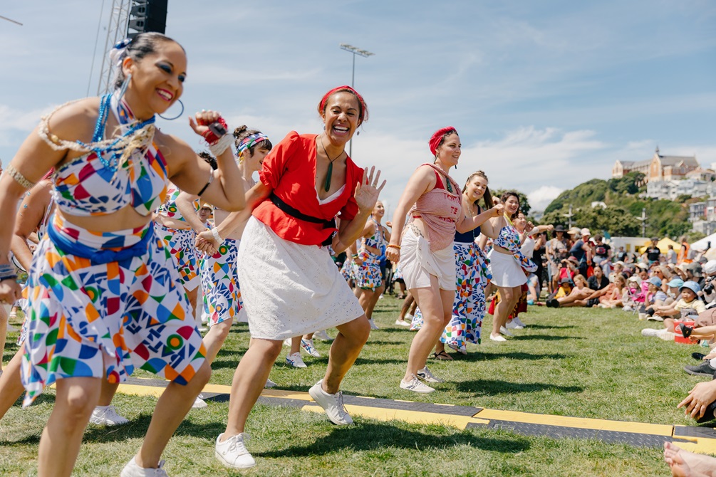 A group of performers dancing in the park in front of a seated crowd.