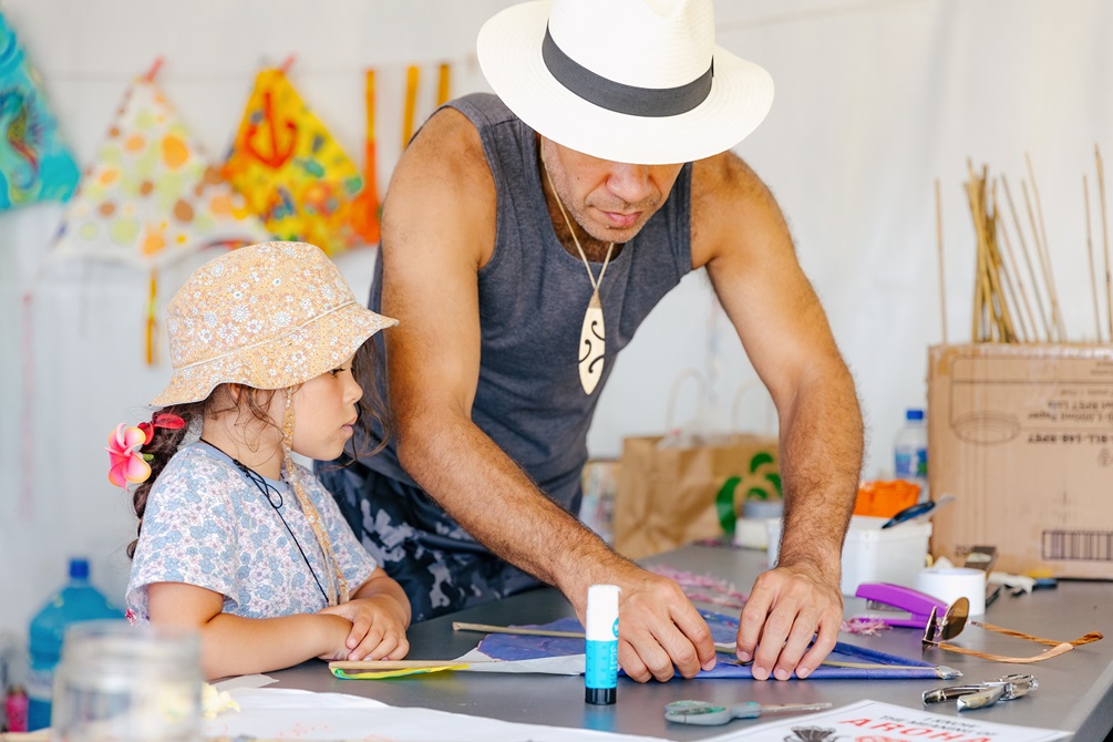 An older man helps a young child build a kite.