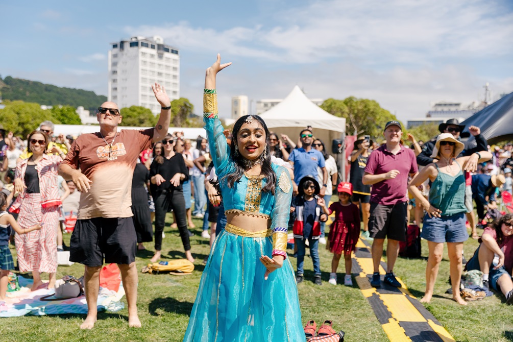 A crowd of people dancing to music. At the front of an image is a young woman in traditional Indian dress.