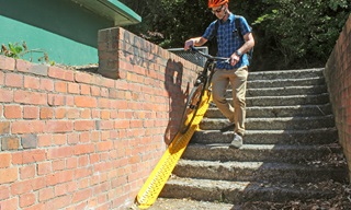 Person walking down stairs pushing their bike, which is rolling along a metal bike ramp which lines the side of the stairs.