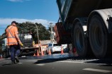 A truck depositing stones onto fresh bitumen.