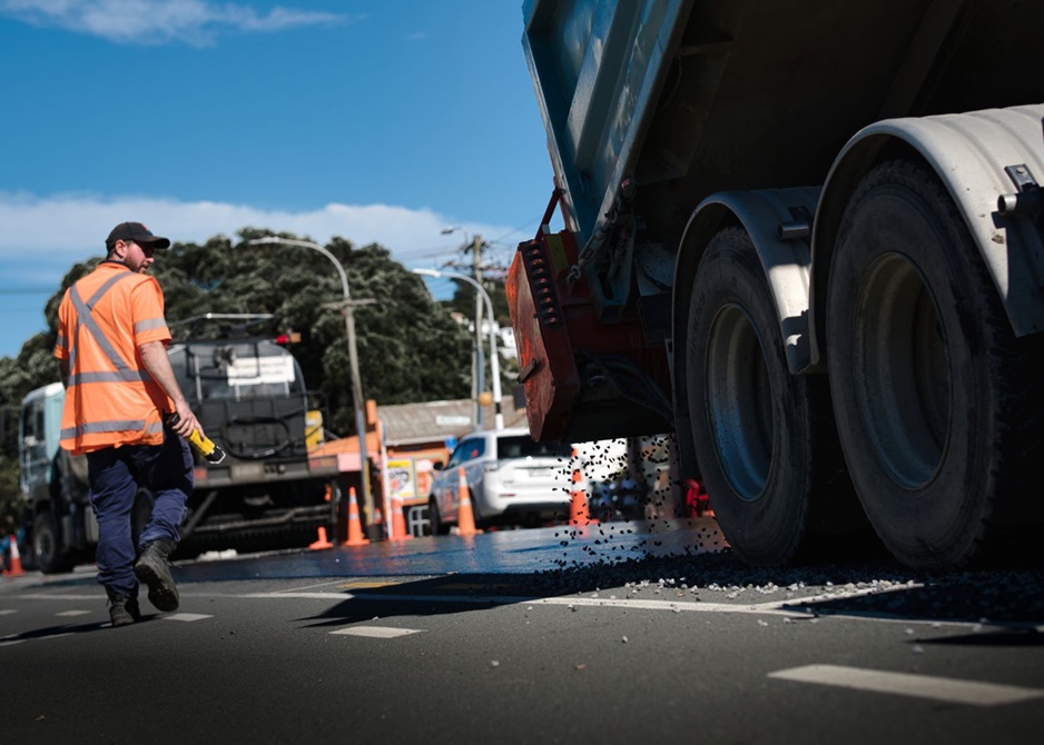 A truck depositing stones onto fresh bitumen.