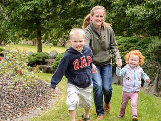 Woman, a boy and a little girl running alongside flower garden.