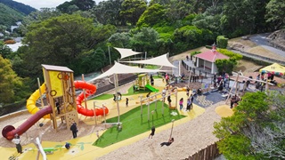 A fort with three slides, one yellow, one red and one crimson. Shade sails, swings and climbing frames.